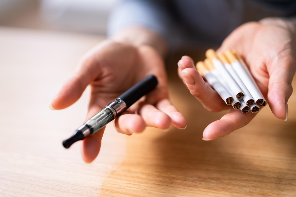 person holding an e-cigarette and cigarettes